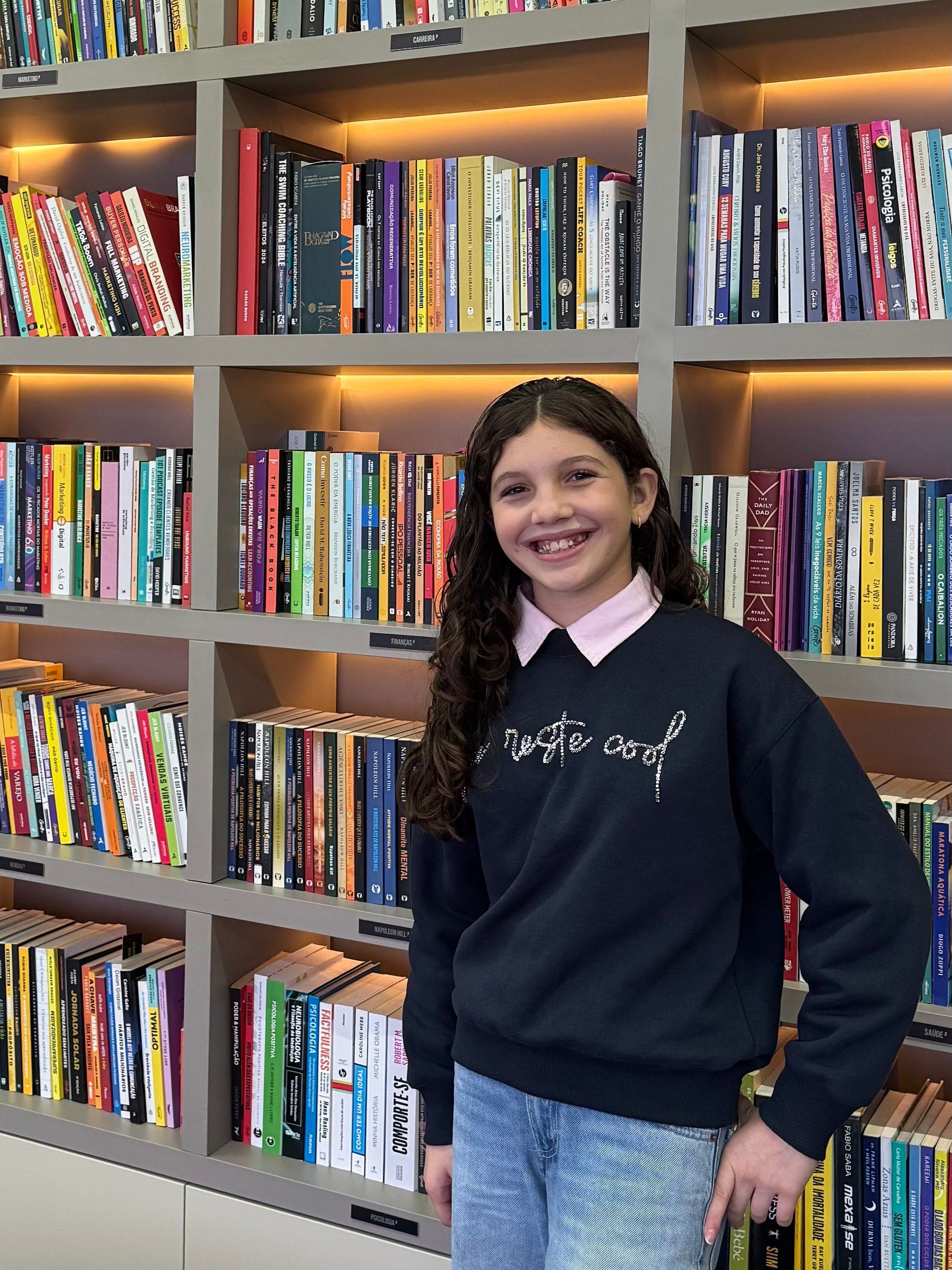 Gabi sorrindo na frente de uma estante cheia de livros