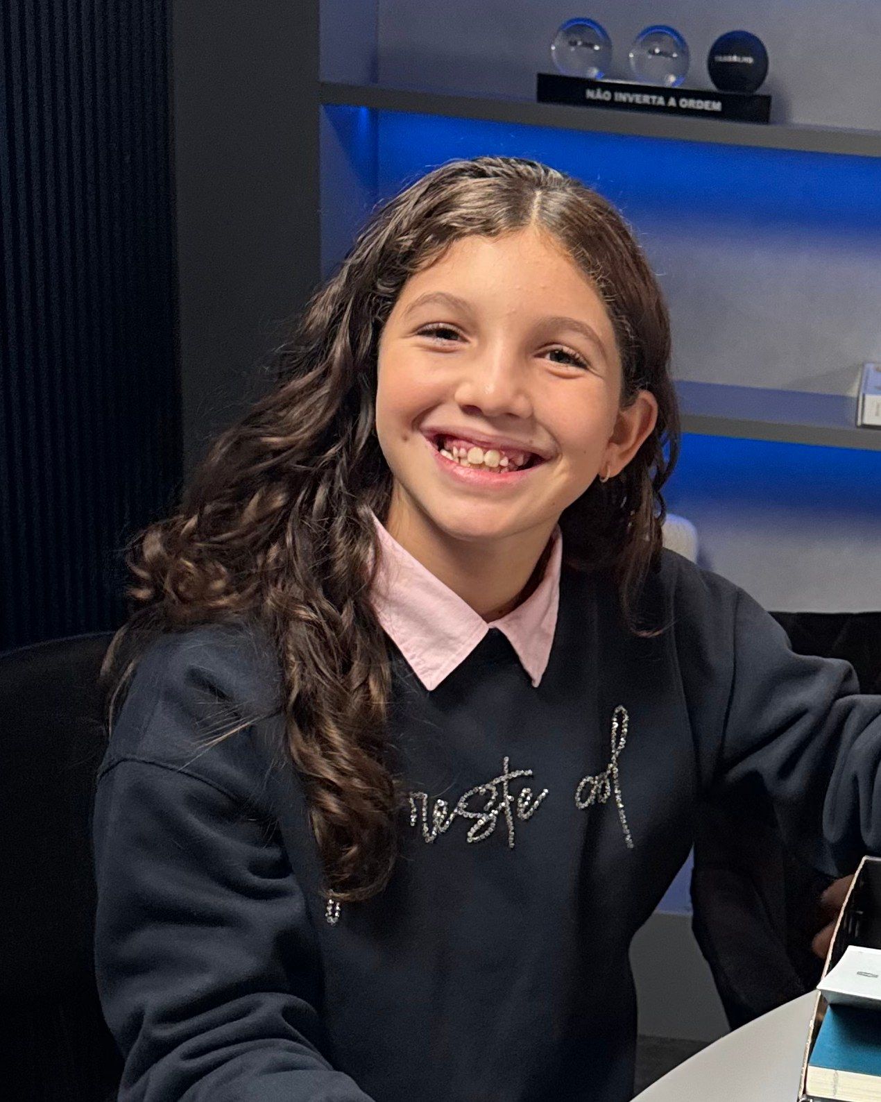 Gabi sorrindo na mesa do estúdio, no dia da gravação do podcast